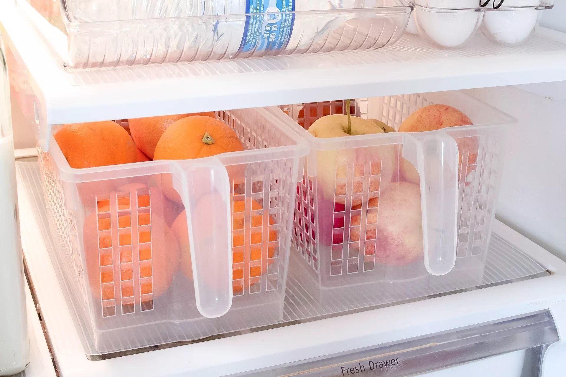 Apples and oranges in small storage baskets inside our fridge with handles for easy pull-out and grab