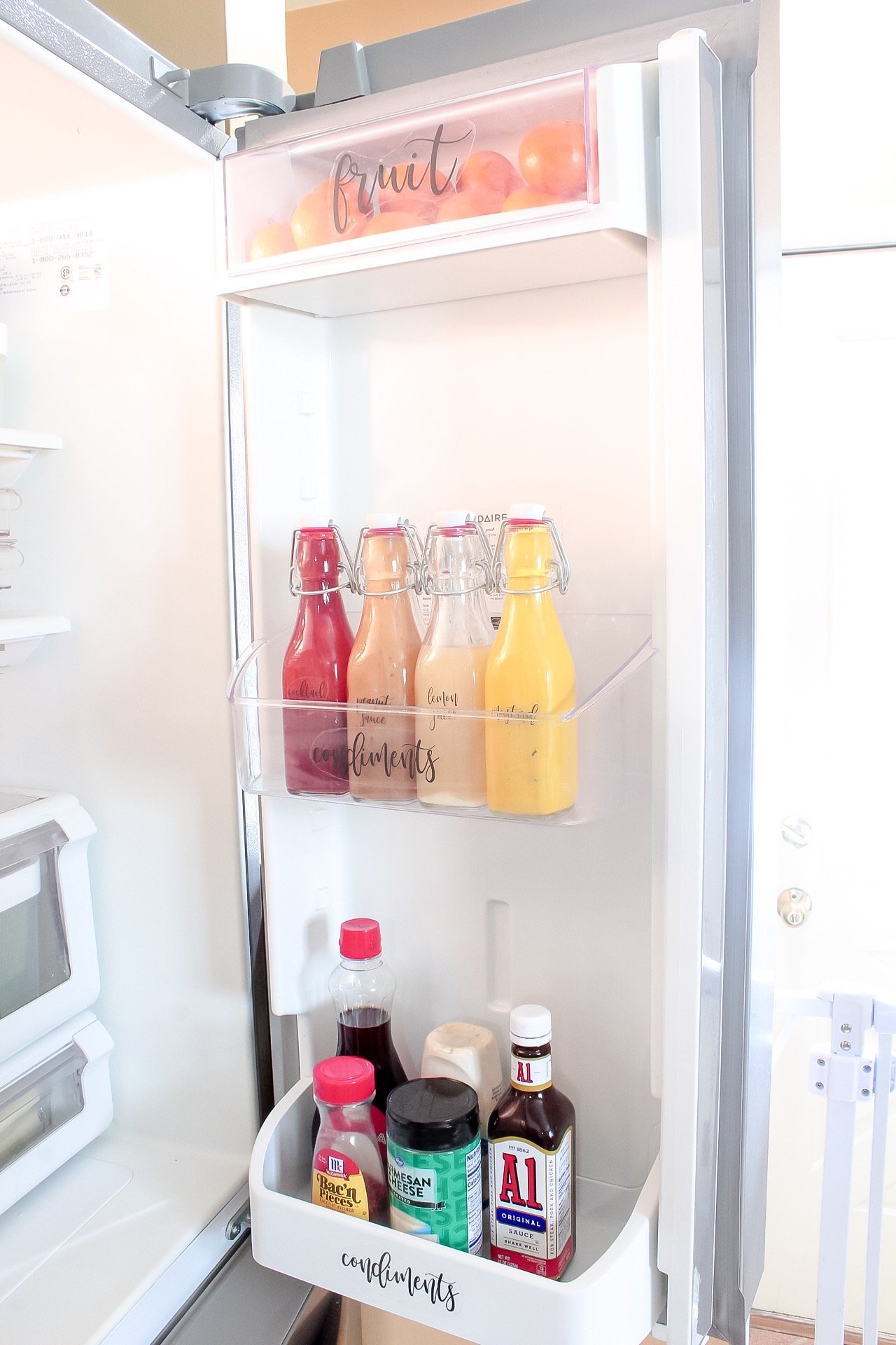 Right fridge door with small oranges in top, condiments in neatly labels bottles, and misc. condiments