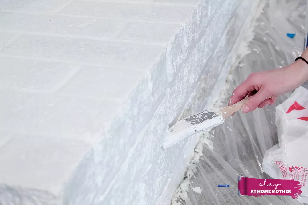 Painting grout lines of brick fireplace with SuperPaint and 2-inch paintbrush in color Extra White