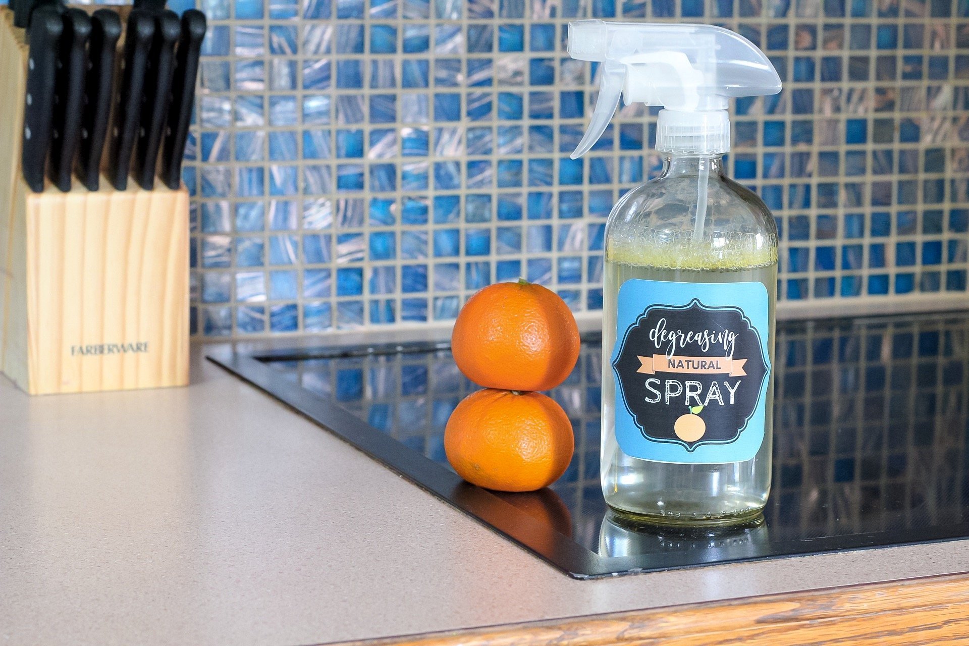 Bottle of homemade greaser with decorative label sitting next to stacked oranges