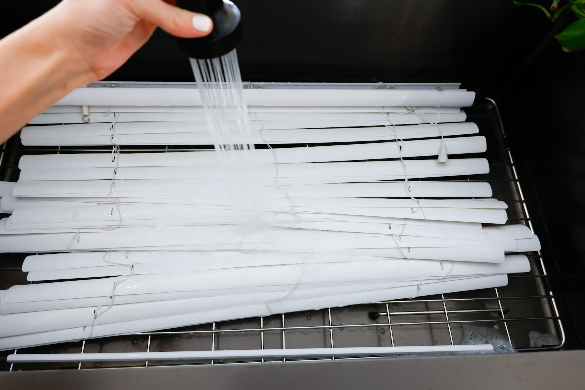 rinsing the soaked blinds with water in the sink